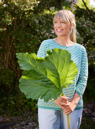 Woman holding a big leaf, covering half her blue knit swetaer